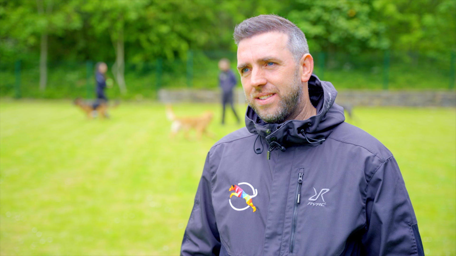 Photo of our head trainer and company founder, Craig Rice, speaking to a journalist (off camera) with 2 dog handlers and dogs in the background, at our secure training centre in sheffield